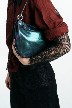 Eine Person, die ein bordeauxfarbenes Hemd mit Spitzenärmeln trägt, hält eine metallisch glänzende, blaugrüne Handtasche von INA KENT unter ihrem Arm.