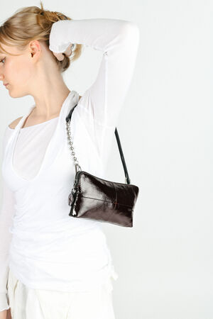 A woman in a white outfit poses with her left arm raised, holding a small, glossy black INA KENT handbag over her shoulder.