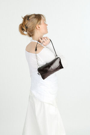 A woman in a white outfit stands sideways, holding a small black INA KENT handbag over her shoulder against a plain light background.