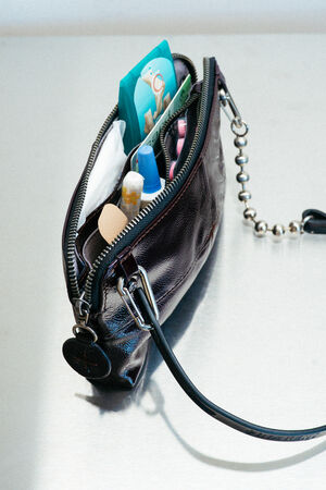 A small black INA KENT zippered pouch is open, revealing tissues, bandages, lip balm, hand sanitizer, and other personal care items inside.