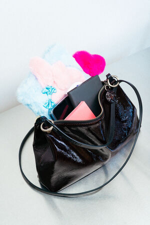 An INA KENT black patent leather handbag contains a blue furry notebook, a pink furry item, a bright pink heart, a black wallet, and a pink envelope.