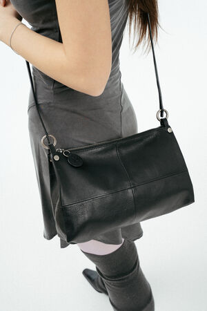 A woman wearing a grey dress and knee-high socks carries an INA KENT black leather shoulder bag with a zipper closure.