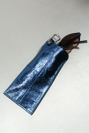 A pair of black cat-eye sunglasses partially inside a metallic blue textured INA KENT pouch with embossed text.