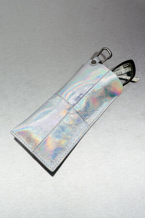 Ein glänzendes, schillerndes INA-KENT-Etui mit Metallverschluss enthält ein schwarz-weißes Motiv, das vor einem grauen Hintergrund teilweise zu sehen ist.