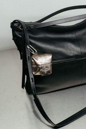 Eine schwarze INA KENT-Handtasche aus Leder mit einem goldfarbenen Mini-Beutel am Riemen, präsentiert auf einem hellen, neutralen Untergrund.