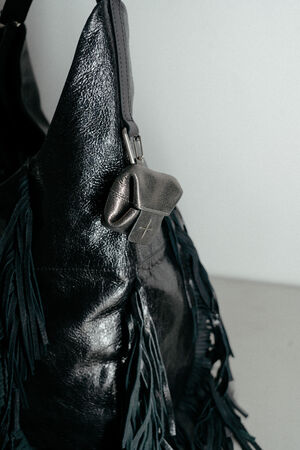 Nahaufnahme einer schwarzen Ledertasche mit Fransen von INA KENT, die mit einem kleinen, fest angebrachten Metallbeutel und silbernen Beschlägen versehen ist, vor einem einfarbigen Hintergrund.