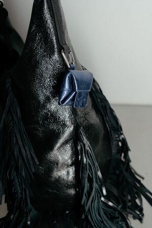 Schwarze Ledertasche mit Fransen von INA KENT, an deren Riemen ein kleines blaues Lederetui befestigt ist, fotografiert vor einem einfarbigen Hintergrund.