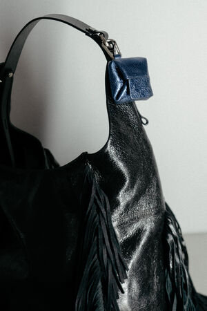 Eine schwarze INA KENT-Tasche aus Leder mit Fransen und einem kleinen blauen Beutel, der am Henkel befestigt ist.