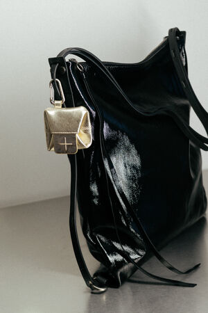 Eine glänzende schwarze INA KENT-Handtasche aus Leder mit einem kleinen goldfarbenen Metallbeutel, der am Riemen befestigt ist, auf einer glatten, hellen Oberfläche.