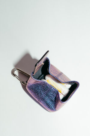 A small, iridescent INA KENT pouch with a keychain clip holds a single tampon inside, set against a plain white background.