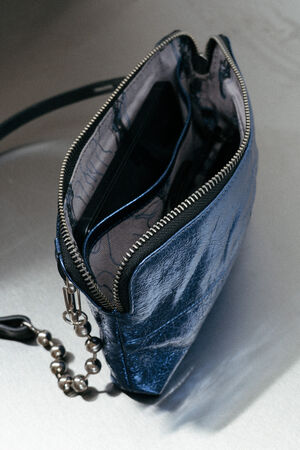 Ein metallisch-blaues Etui mit Reißverschluss von INA KENT und Handschlaufe, das teilweise geöffnet ist und den Blick auf eine schwarze Geldbörse oder ein Kartenetui im Inneren freigibt.