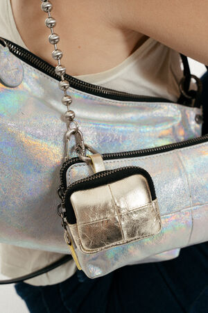 Nahaufnahme einer Person, die ein weißes Tanktop trägt und eine glänzende, schillernde INA KENT-Handtasche sowie ein kleines, goldfarbenes Metalltäschchen am Riemen der Tasche bei sich hat.