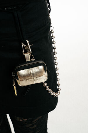 An einem schwarzen Rock ist ein kleines, metallisch-goldenes INA KENT-Täschchen mit Reißverschluss befestigt; der Rock wird durch eine silberne Perlenkette und Strumpfhosen mit Spitzenmuster ergänzt.