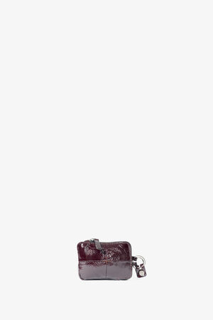 Small, rectangular, dark burgundy leather coin pouch by INA KENT with zipper closure and a metal keychain attachment, shown against a plain white background.