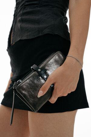 A person wearing a black skirt and top holds an INA KENT metallic black wallet in their right hand.