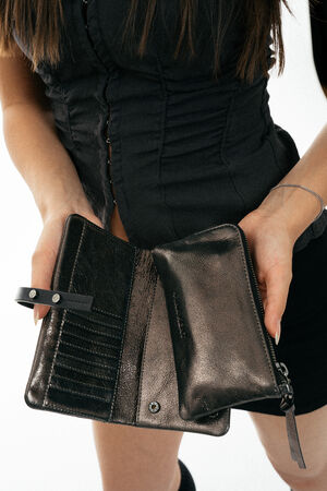 A person in a black outfit holds open an empty black leather wallet by INA KENT, showing its compartments and card slots.