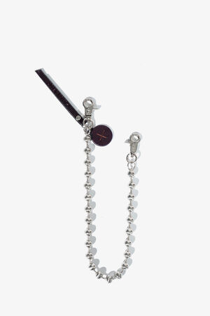 A silver beaded chain with two lobster clasps, a round black charm with an X, and a black rectangular tag attached—an understated accessory by INA KENT.