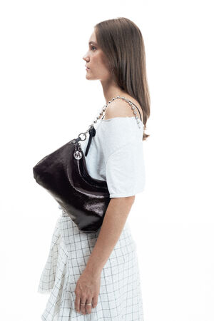 Woman standing in profile, wearing a white top and plaid skirt, carrying a large black INA KENT shoulder bag with metal hardware.