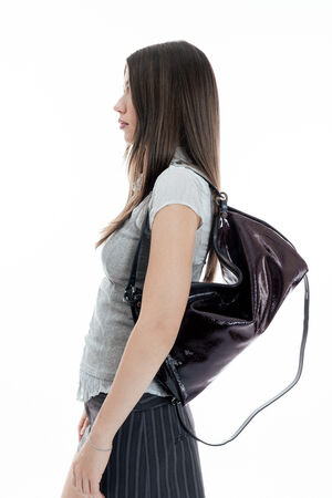 Woman in a light grey blouse and striped skirt standing in profile view, carrying a large black INA KENT leather bag over her shoulder on a white background.