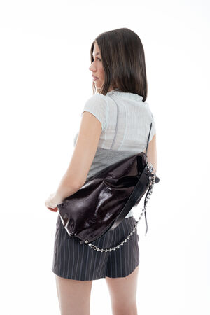 Woman in a short-sleeve blouse and striped skirt facing away, carrying a large, shiny black INA KENT handbag with a chain strap over her shoulder against a white background.