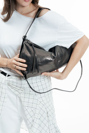 A woman in a white shirt holds a large, shiny black INA KENT handbag under her arm, with a plaid shirt tied around her waist against a white background.