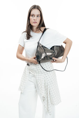 Woman in a white t-shirt and pants with a plaid shirt tied at her waist, holding an INA KENT metallic shoulder bag against a plain white background.