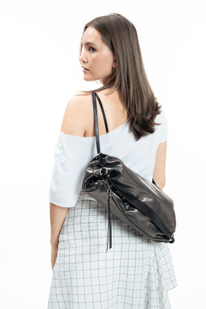 Woman with straight brown hair wearing a white off-shoulder top and checkered skirt, carrying an INA KENT black leather bag over one shoulder, standing against a white background.