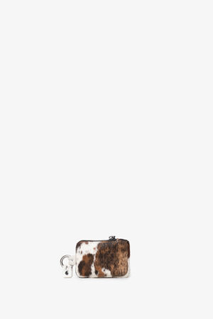 Small rectangular INA KENT wallet with a brown and white fur pattern, silver zipper, and matching keychain tag, displayed on a plain white background.