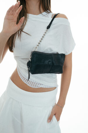 Woman wearing a white outfit and carrying an INA KENT black, furry shoulder bag with a chain strap, one hand raised and her face partially out of frame.