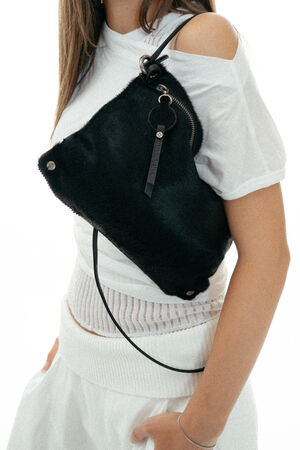 A person in a white outfit carries an INA KENT black textured crossbody bag with a zipper and keychain detail over their shoulder.