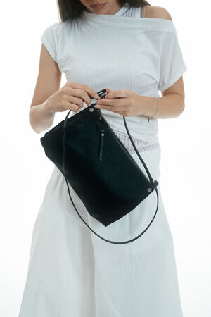 Woman in a white outfit holds and opens an INA KENT black shoulder bag against a plain white background.