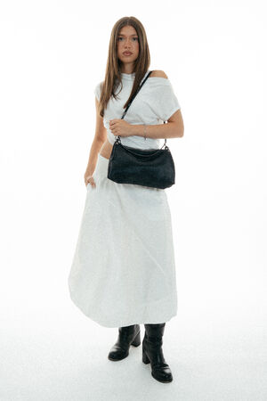 Woman standing in a white dress and black boots, holding an INA KENT black shoulder bag, against a plain white background.
