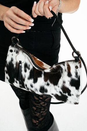 A person holds an INA KENT cow-print handbag with a zipper, wearing a black skirt, lace leggings, and boots.