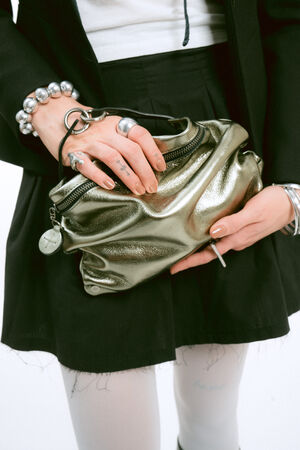 A person in a black blazer and skirt holds a metallic olive-green clutch bag.