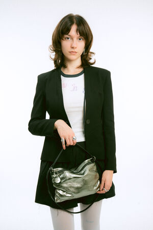 A person wearing a black blazer over a white t-shirt, holding a metallic silver handbag.