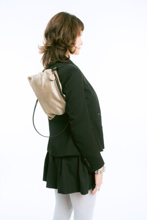 A person wearing a black blazer and skirt carries a small, metallic beige crossbody bag on their back.