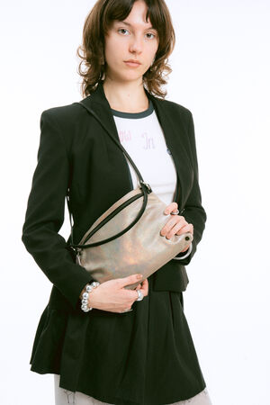 A person wearing a black blazer holds a shimmering, metallic-toned crossbody bag with a black zipper.