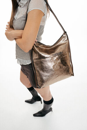 A metallic bronze INA KENT hobo-style shoulder bag worn by a person.