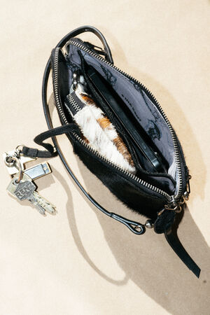 A small open black purse showing keys, a phone, and a striped wallet inside, placed on a light tan surface.