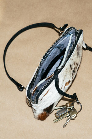 A small animal print handbag with a zipper partially open, revealing the interior, with a set of keys attached to the zipper pull, on a tan surface.