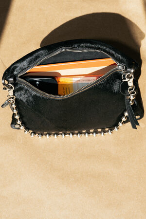 A black handbag with a silver chain strap lies open, revealing books, a smartphone, and other small personal items inside against a tan background.