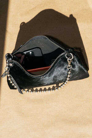 A black leather purse with a silver chain strap is open, revealing a smartphone and a red item inside, on a brown surface.