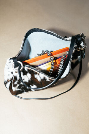 A small, open handbag with a black and white animal print pattern, containing an orange book and a silver beaded chain, is placed on a beige surface.