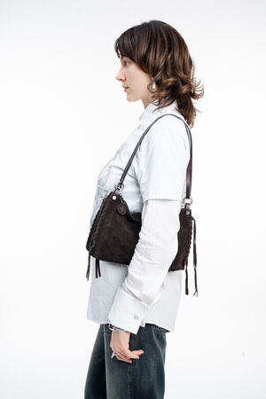 A person in a white button-down shirt wearing an INA KENT brown suede shoulder bag with tassel details.