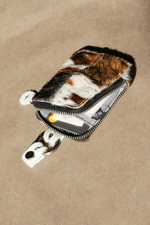 A small, zippered pouch with a fur-like exterior holds cards and a key, placed on a plain beige surface.